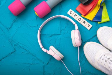 Spor ayakkabıları, halterler, lastikler, kulaklıklar mavi arka planda.