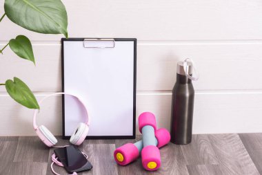 Dambıllar, not panosu, kulaklıklar ve cep telefonu, yeşil yapraklar ve bir şişe su - evde egzersiz