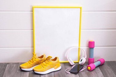 Evde egzersiz - dambıllar ve sarı spor ayakkabılar, sarı çerçeveli bir tabela, notlar, kulaklıklar ve cep telefonu için, hepsi beyaz arka planda, yakın plan