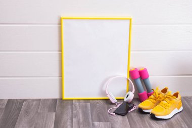 Tahta, dambıl, sarı spor ayakkabı, kulaklık ve cep telefonu beyaz arka planda.