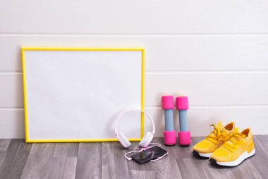 Tahta, dambıl, sarı spor ayakkabı, kulaklık ve cep telefonu beyaz arka planda.