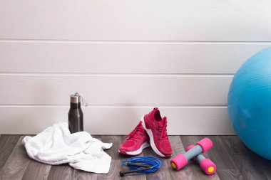 Evde spor - pembe spor ayakkabıları, dambıllar, ip atlama, top ve daha fazlası beyaz arka planda.