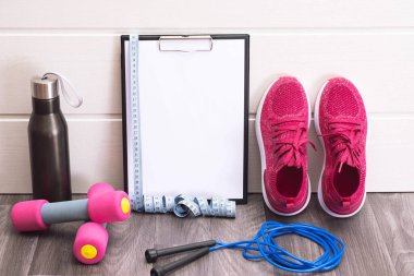 Spor ekipmanları - pembe spor ayakkabıları, dambıllar, ip atlama ve isim plakası, mezura ve siyah su şişesi, yakın plan.