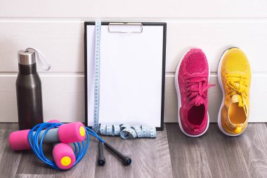 Spor ekipmanları - pembe ve sarı spor ayakkabılar, dambıllar, atlama ipi ve plaka, mezura ve siyah su şişesi, yakın çekim