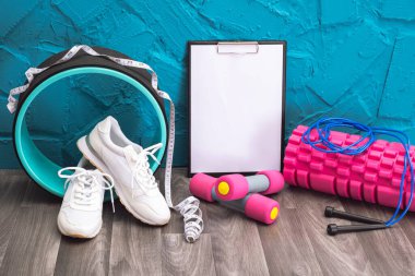 Evde egzersiz - beyaz spor ayakkabıları, dambıllar, ip atlama, mezura, not panosu ve masaj silindiri, yakın plan ve mavi arka plan