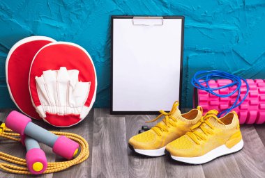 Sarı spor ayakkabılar, dambıllar, ip atlama, tahta ve masaj silindiri, yakın plan ve mavi arka plan.