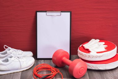 Evde egzersiz - kırmızı halterler, ip atlama ve tekme pedleri, not panosu ve beyaz spor ayakkabılar, yakın plan ve kırmızı arka plan
