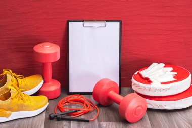 Evde egzersiz - kırmızı halterler, ip atlama ve tekme pedleri, not panosu ve sarı spor ayakkabılar, yakın plan ve kırmızı arka plan