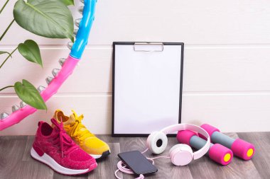 çok renkli spor ayakkabılar, dambıllar, tahta, kulaklık ve cep telefonu, yeşil büyük yapraklar, beyaz arka planda.