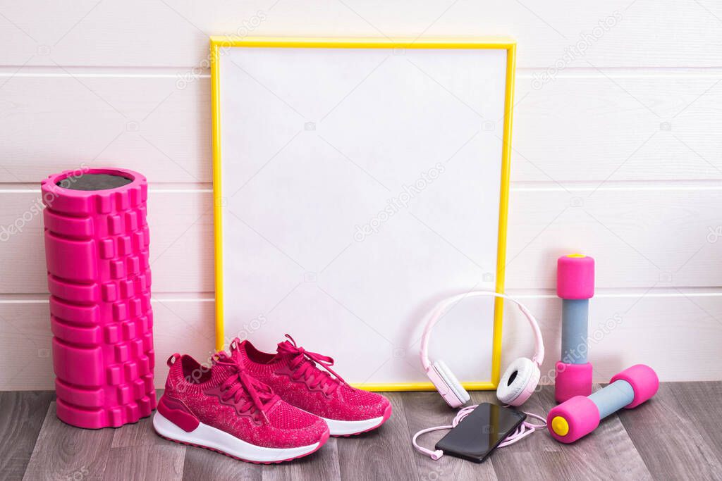 sports at home - dumbbells and pink sneakers, massage roller, plate, with a yellow frame, for notes, headphones and a cell phone on a white background