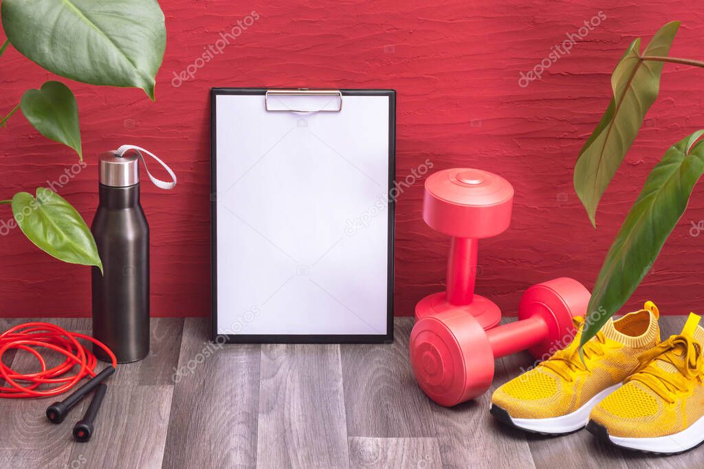 red dumbbells and yellow sneakers, water bottle and jump rope, note board and large green leaves, on a red background