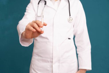 Doktor bir steteskopun omuzlarında elinde aşıyla bir şırınga tutuyor, mavi bir arka planda.