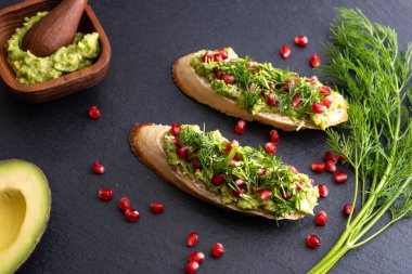 Lezzetli avokado kanepeleri olgun nar tohumları, susam tohumları ve mis kokulu taze dereotu, siyah arka plan ve yakın plan serpiştirilmiş.