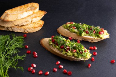 Lezzetli avokado atıştırmalıkları, olgun nar tohumları serpiştirilmiş susam tohumları ve mis kokulu taze dereotu, siyah arka plan