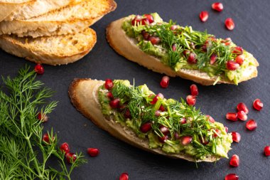 Lezzetli avokado kanepeleri olgun nar tohumları, susam tohumları ve mis kokulu taze dereotu, siyah arka plan ve yakın plan serpiştirilmiş.