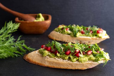 Lezzetli ve sağlıklı bir atıştırmalık - avokado, olgun nar tohumları serpiştirilmiş, susam tohumları ve mis kokulu taze dereotu, siyah arka plan ve yakın plan