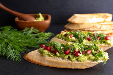 Atıştırmalık - avokado, olgun nar tohumları serpiştirilmiş, susam tohumları ve mis kokulu taze dereotu, siyah arka plan ve yakın plan