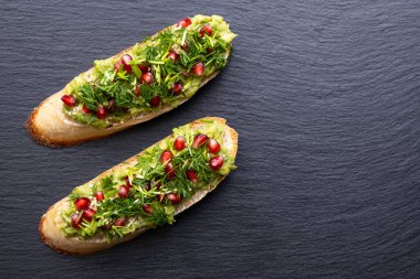 İki aperatif - avokado, olgun nar tohumları serpiştirilmiş, susam tohumları ve mis kokulu taze dereotu, siyah arka plan ve yakın plan