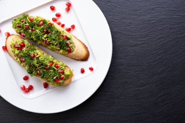 Aperatifler beyaz bir tabakta - avokado, olgun nar tohumları serpiştirilmiş, susam tohumları ve taze dereotu, yakın çekim