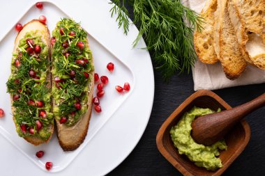 Bir tabakta sağlıklı atıştırmalıklar - avokado, olgun nar tohumları serpiştirilmiş susam tohumları ve taze dereotu, yakın çekim