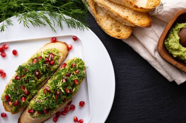 Masada sağlıklı atıştırmalıklar, avokado, olgun nar tohumları serpiştirilmiş susam tohumları ve taze dereotu, yakın çekim.