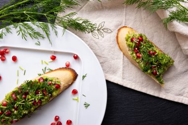 Avokado, nar ve dereottan yapılmış iki sağlıklı atıştırmalık. Biri ısırılmış.