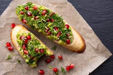 Siyah bir arka planın ortasında, parşömen kağıdında bir ısırık ve bir aperatif avokado, nar tohumu ve dereotu var. Yakın plan.