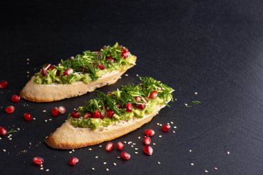 İki adet avokado ve olgun nar tohumu, susam tohumu ve aromatik dereotu siyah bir zemin üzerinde.