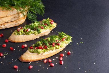 Siyah arka planda avokado ve olgun nar tohumları, susam tohumları ve aromatik dereottan oluşan bir atıştırmalık.