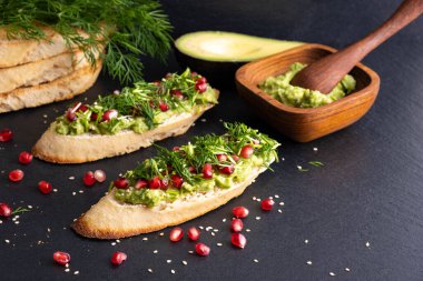 Siyah bir arka planda püre avokado ve olgun nar taneleri, susam tohumları ve aromatik dereottan oluşan bir atıştırmalık.