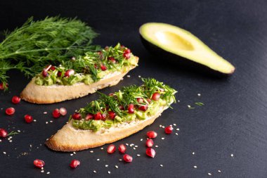 Siyah bir arka planda, püre avokado ve olgun nar tohumları, susam tohumları ve aromatik dereottan oluşan bir atıştırmalık.