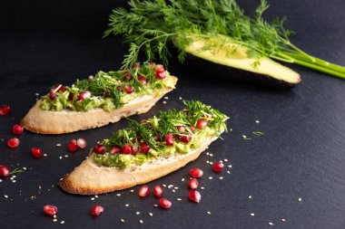 Sağlıklı çerez - püre avokado ve olgun nar tohumları, susam tohumları ve aromatik dereotu, siyah bir arka planda, yakın plan