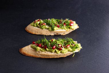 Sağlıklı çerez - püre avokado ve olgun nar tohumları, susam tohumları ve aromatik dereotu, siyah bir arka planda, yakın plan