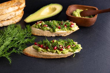 Avokado ve olgun nar tohumları, susam tohumları ve aromatik dereottan oluşan siyah bir arka planda, yakın plan, sağlıklı bir tepe örtüsü.