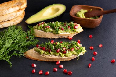 Kanepeler - avokado, olgun nar tohumları, susam tohumları ve aromatik dereotu, siyah arka planda, yakın planda.