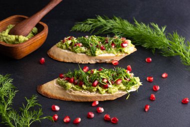 avokado püresi, olgun nar tohumları, susam tohumları ve mis kokulu taze dereotu filizleri - kızarmış ekmek ve siyah bir zemin üzerine serilmiş.