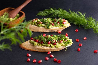 Avokado püresi, olgun nar tohumları, susam tohumları ve taze dereotundan oluşan mis kokulu baharatlar, siyah arka plan.