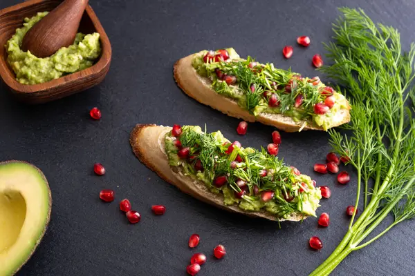 Lezzetli avokado kanepeleri olgun nar tohumları, susam tohumları ve mis kokulu taze dereotu, siyah arka plan ve yakın plan serpiştirilmiş.