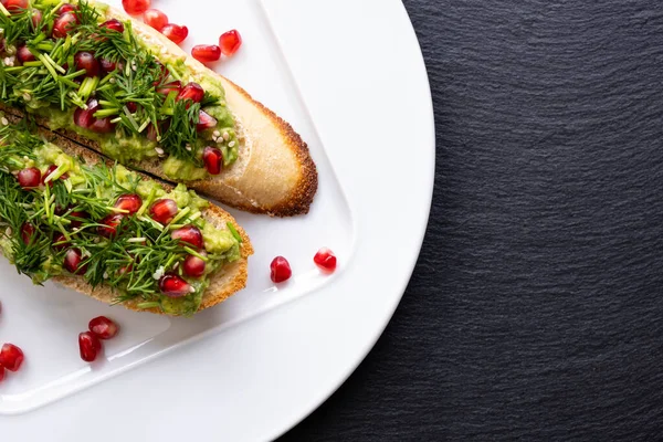 Beyaz bir tabakta iştah açıcı atıştırmalıklar - avokado, olgun nar tohumları serpiştirilmiş, susam tohumları ve taze dereotu, yakın çekim