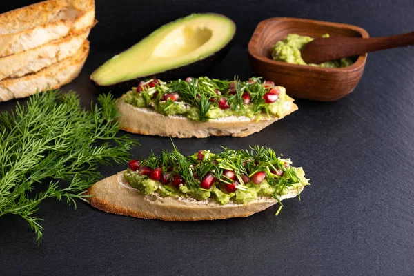 Avokado ve olgun nar tohumları, susam tohumları ve aromatik dereottan oluşan siyah bir arka planda, yakın plan, sağlıklı bir tepe örtüsü.