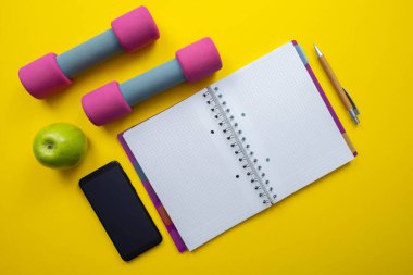 Cep telefonu, pembe dambıllar, defter ve kalem, yeşil elma ve sarı arka plan.