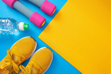 sarı spor ayakkabılar ve sarı paspas, dambıllar, bir şişe su, mavi arka plan