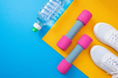 sarı hasırlar ve pembe dambıllar, beyaz spor ayakkabılar ve bir şişe su, mavi arka plan ve yakın plan