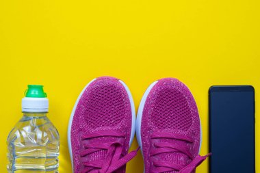 Koşu için. Pembe ayakkabılar, bir şişe su ve sarı arka planda bir cep telefonu.