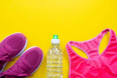 Pembe spor ayakkabılar ve kolsuz tişört, sarı arka planda su şişesi.