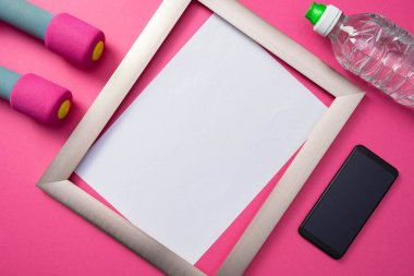 Metal çerçeve, cep telefonu ve su şişesi, halterler ortak pembe arka planda yatıyor.