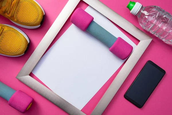 sports at home - yellow sneakers, a metal frame, a cell phone and a bottle of water, dumbbells lie on a common pink background