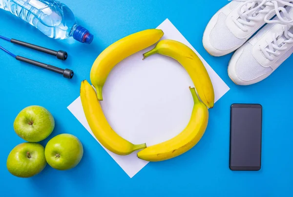 bananas in the center, water and apples, jump rope and white sneakers, cell phone on a blue background