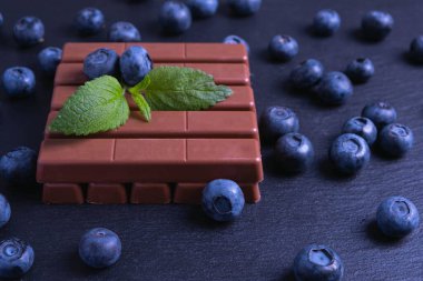 Çizgili çikolata ve siyah arka planda serpiştirilmiş yabanmersini