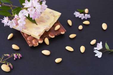 bars of milk and white chocolate with almond nuts on a black background with decorative almond flowers